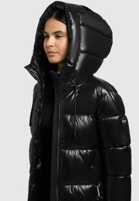 Sort puffjakke med blank overflade, der har en stor hætte, trykknaplukning foran og sidelommer. Tekstureret quiltet design.