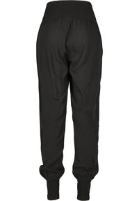 Pantalon noir taille haute avec taille et poignets élastiqués smockés, en tissu lisse, vu de dos.