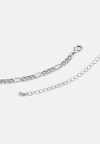 Catena in metallo argentato con anelli ovali e chiusura a moschettone, accompagnata da una seconda catena con anelli circolari e estremità a sfera.