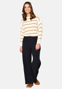 Cream sweater with gold stripes, paired with navy wide-leg pants and tan slippers. Soft texture, relaxed fit, and casual style.