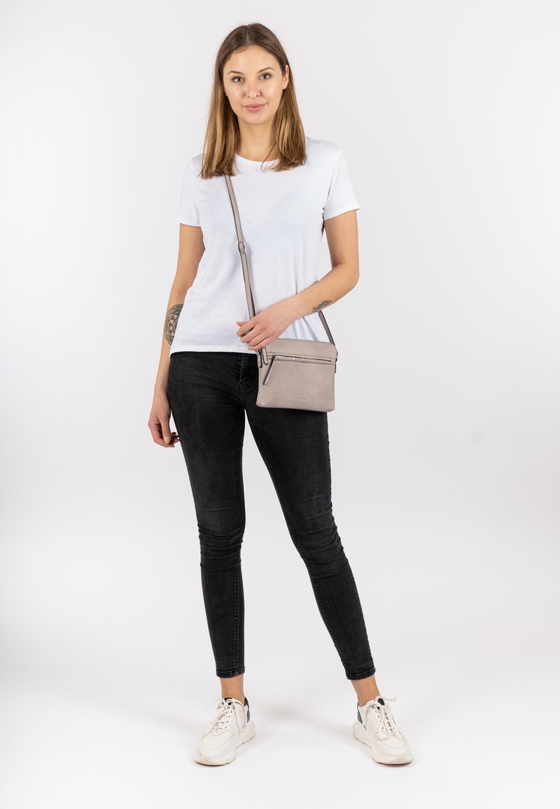 White crew-neck t-shirt, black skinny jeans, and white sneakers. Small gray crossbody bag with zipper detail. Plain background.