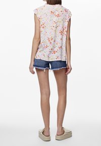 Hedvábná bezrukávová blůza s květinovým vzorem v pastelových barvách, s volánovými rameny. Kombinována s džínovými šortkami a sandály na platformě.