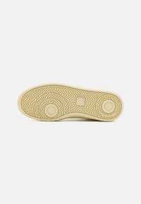Sula på en sneaker, med en strukturerad yta med fiskbensmönster, i en mjuk beige färg, med cirkulära designelement.