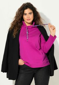 Felpa fucsia con collo a sacco e lacci decorativi, abbinata a un blazer nero e jeans in denim scuro. Tessuto morbido con una vestibilità rilassata.