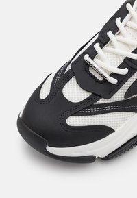Black and white sneaker featuring mesh material, textured rubber sole, and tonal stitching. Silver hardware with brand name accent.