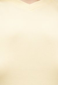 Κοντινό πλάνο ενός ατόμου που φοράει ανοιχτόκίτρινη ριπ μπλούζα με V-λαιμόκοψη, εμφανίζοντας το λαιμό και το πάνω μέρος του στήθους.