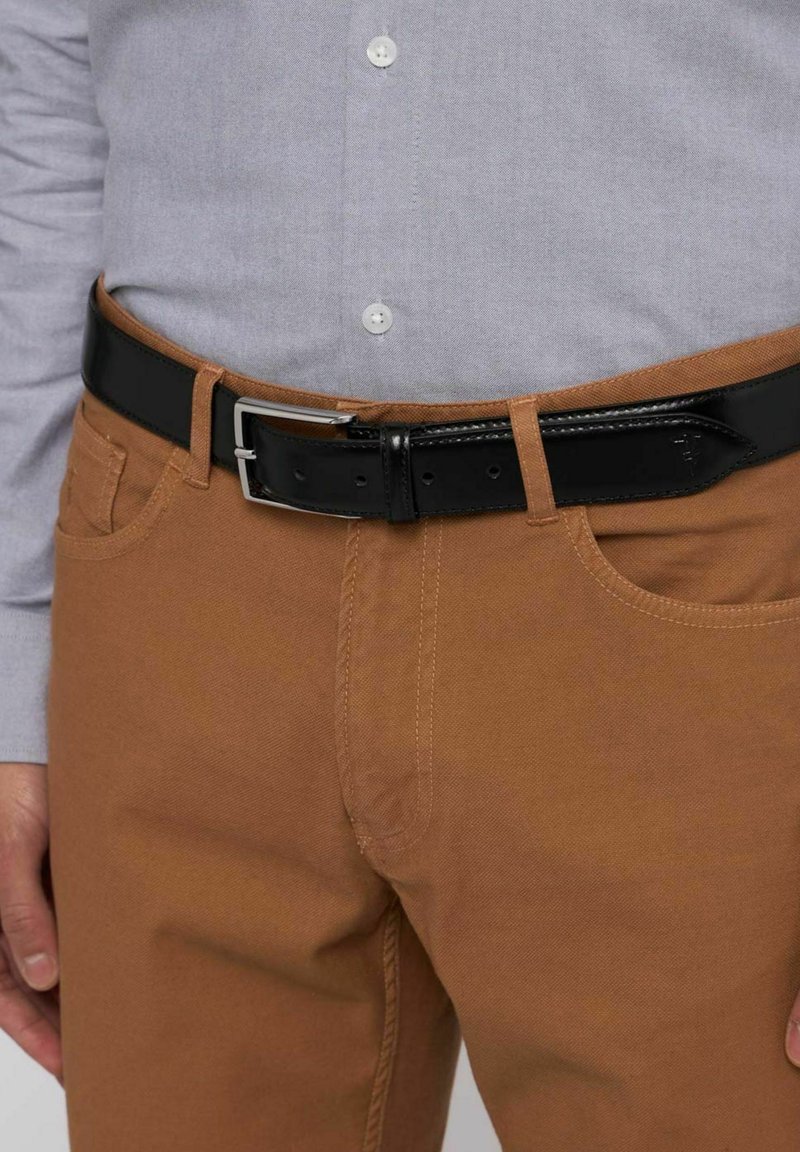 Brązowe bawełniane chinosy z bocznymi kieszeniami, noszone z jasnoszarą koszulą i czarnym skórzanym paskiem z srebrną klamrą.