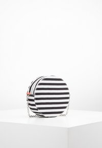 Pyöreä laukku mustavalkoraitaista kangasta, jossa on vetoketjusuljenta ja hopeinen ketjuhihna olkapäälle tai ristivartalolle.