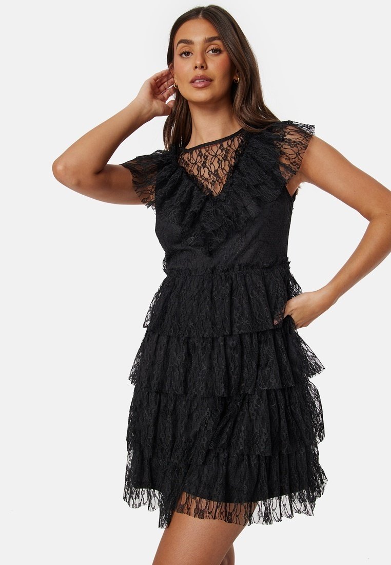 Robe noire en dentelle avec un design superposé, des manches volantes et un décolleté en V, mettant en valeur des motifs complexes et une finition texturée.