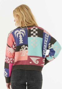Pullover aus mehrfarbigem gestricktem Muster. Hat übergroße Ärmelsäume, gerippte Säume und Designs wie Palmen und geometrische Formen.