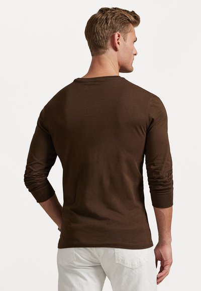 Brown long-sleeve shirt made of soft fabric, featuring a round neckline and fitted sleeves, worn with light-colored pants.