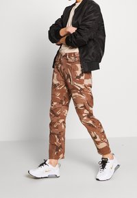 Bruine camouflagebroek met een rechte pasvorm, gemaakt van stevig materiaal. Gecombineerd met een zwarte bomberjack en witte sneakers.