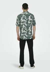 Cămașă pentru bărbați cu mânecă scurtă, de culoare albă, cu imprimeu de frunze tropicale verzi. Asortată cu pantaloni negri și adidași albi. Cămașa are o croială lejeră.
