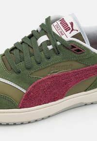 Puma sneakers featuring a green suede upper, maroon textured accent, white midsole, and black eyelets with green laces.