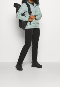 Light teal pullover jacket with a hood, black backpack, black slim pants, and black athletic shoes. Smooth fabric with minimal design details.