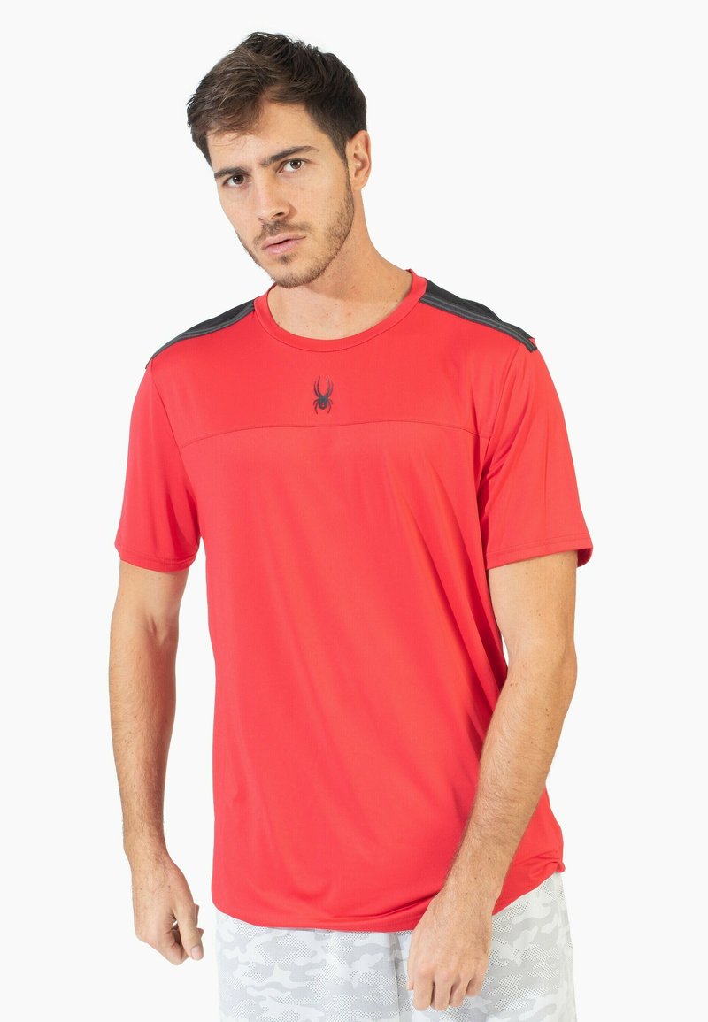 Camiseta deportiva roja hecha de un tejido ligero. Presenta mangas cortas, cuello redondo, acentos negros en los hombros y un pequeño logo de araña en el pecho.