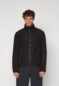 Veste en polaire noire avec un col montant, fermeture éclair frontale et poches latérales. Caractérisée par une texture lisse et un design minimaliste.