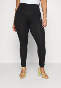 Leggings noires taille haute en tissu extensible, avec un design ajusté et un petit détail de logo blanc à la hanche.