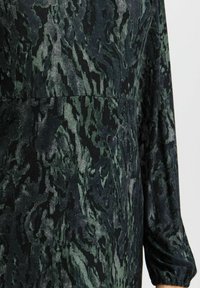 Långärmad klänning i texturerat tyg med ett mörkgrönt och svart abstrakt mönster, som har en figurnära midja och samlade ärmar.