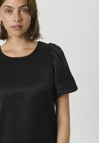 Čierny saténový top s okrúhlym výstrihom a mierne nariasenými krátkymi rukávmi, hladká štruktúra s lesklým povrchom a minimalistickým dizajnom.