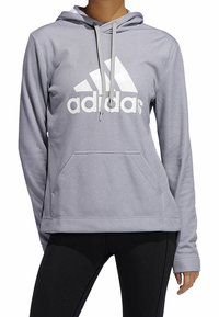 Sweat à capuche gris en tissu texturé, avec une poche avant, une capuche à cordon et un grand logo Adidas blanc sur la poitrine.