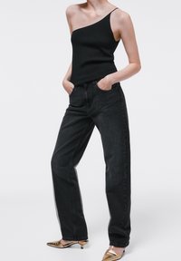 Top a costa nera a costine con una spalla abbinato a jeans neri larghi. Mules dorati con punta affilata. Design semplice e moderno.