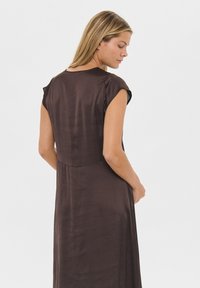 Smeđi haljina bez rukava s laganim sjajem, koja ima usku korzet i nabrani struk, glatku teksturu i jednostavnu, elegantnu siluetu.