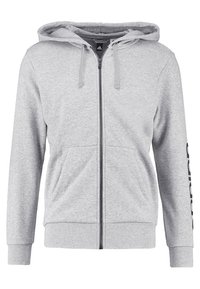 Sweat à capuche zippé gris en tissu doux, avec une capuche, des poches avant et un logo imprimé le long de la manche gauche. Coupe et design décontractés.