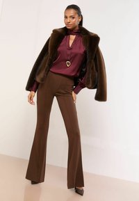 Bluză din satin vișiniu cu guler cu fundă, pantaloni evazați maro și o capă maro din blană artificială. Accesorizată cu un colier auriu cu pandantiv și pantofi cu toc ascuțit.