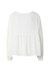 Blouse blanche à manches longues avec couture froncée sous les omoplates et poignets élastiques, vue de dos sur fond uni.