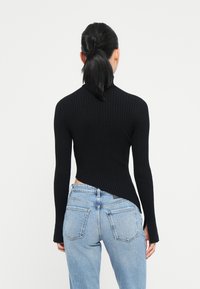 Top lungo a maniche ribbato nero con un design aderente, caratterizzato da un collo alto e un orlo asimmetrico, abbinato a jeans di denim azzurri a vita alta.