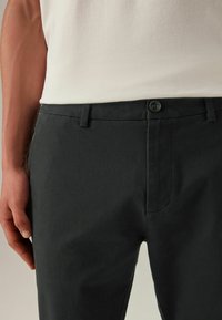 Dunkelgraue Baumwoll-Chinos mit glatter Textur, mit einem vorderen Knopfverschluss, Gürtelschlaufen und einem dezenten Bügel vorne.