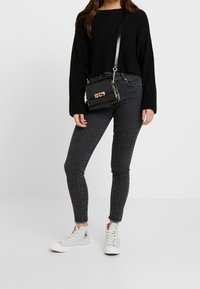 Svart stickad kort tröja, grå leopardmönstrade tajta jeans och ljusa högtoppsskor. Liten svart axelväska med metalldetaljer.