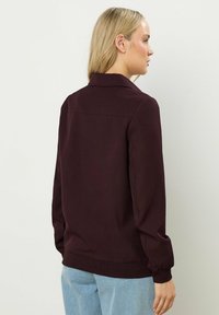 Bordeaux jack met een kraag, lange mouwen en elastische manchetten, met een gladde textuur en minimalistisch ontwerp.