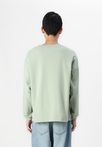 Lichtgroen overhemd met lange mouwen van katoen, met een ronde hals en een losse pasvorm. Gecombineerd met lichtblauwe denim jeans.