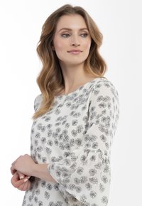 Blomstret bluse med lange, klokkeformede ærmer. Hvidt stof med små sorte blomstermønstre. Rund halsudskæring, let tekstur.