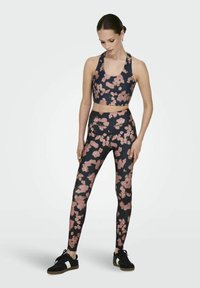 Sportski grudnjak i tajice s cvjetnim uzorkom u tamnoplavoj boji s svijetlo ružičastim naglascima. Elastična tkanina i tijesni kroj. Crne atletske tenisice.