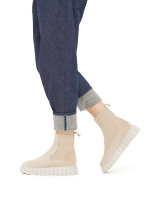 Bottines beiges en daim avec une semelle en caoutchouc blanche épaisse. Elles ont des panneaux latéraux, des languettes et sont associées à un jean en denim retroussé.