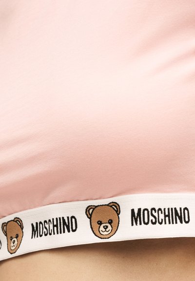 Ροζ ύφασμα με λευκή ελαστική ταινία που εμφανίζει επαναλαμβανόμενα καφέ πρόσωπα αρκουδάκια και το όνομα της μάρκας "MOSCHINO" με μαύρο κείμενο.