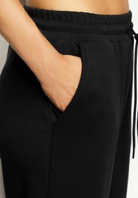 Joggers neri con vita regolabile, dotati di tasche laterali e una texture liscia e morbida. Il tessuto sembra elastico e leggero.