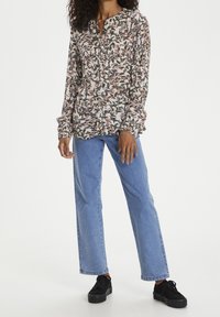 Blusa a maniche lunghe con motivo floreale nei toni di rosa, verde e crema, abbinata a jeans dritti azzurri e sneaker nere.