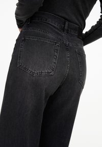 Black denim jeans with a high waist, featuring two back pockets and a smooth texture, shown from a side angle.