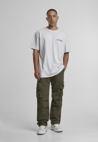 Gray oversized t-shirt, olive cargo pants with multiple pockets, and white sneakers with yellow accents. Simple design and relaxed fit.