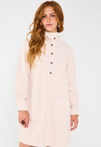Abito in corduroy rosa chiaro con colletto alto, chiusura a bottoni sul davanti, due grandi tasche e maniche lunghe. Tessuto testurizzato e bottoni a contrasto.