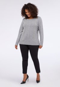 Šedý pletený svetr s texturovanými vertikálními liniemi, kulatým výstřihem, dlouhými rukávy, doplněný o černé přiléhavé kalhoty a černé lodičky s špičatou špičkou.