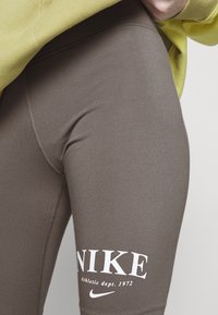 Bruna leggings i stretchmaterial med vitt "NIKE"-logotyp och text, med hög midja och platta sömmar.
