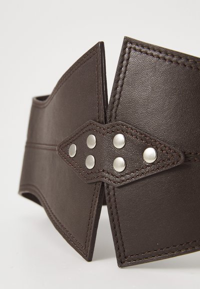 Cinturón de cuero marrón con un acabado texturizado, que presenta tachuelas plateadas y costuras en contraste. Forma puntiaguda única en ambos extremos.