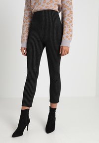 Höga svarta byxor med randig struktur och tapered passform, ihop med svarta ankelboots och en ljus mönstrad tröja.