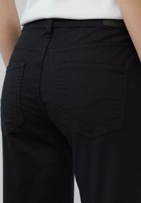 Czarne dżinsy o dopasowanym kroju, z dwiema tylnymi kieszeniami i subtelnym wzorem falistych przeszyć na krawędziach kieszeni. Gładka tekstura.