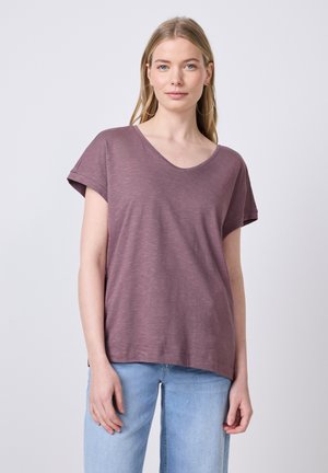 Paarse V-hals T-shirt gemaakt van zachte, lichte stof met opgerolde korte mouwen en een losse pasvorm. Gecombineerd met lichtblauwe jeans.
